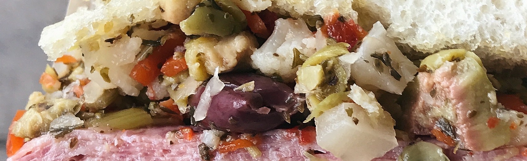 A close-up of muffuletta olive salad — chopped green and Kalamata olives, red peppers, giardiniera and herbs
