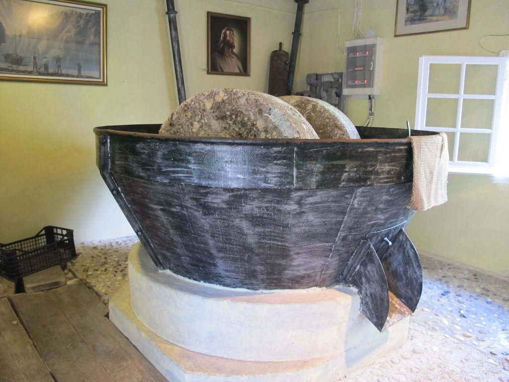 Two large stone crushing wheels standing in a metal basin inside a preserved Greek olive mill.