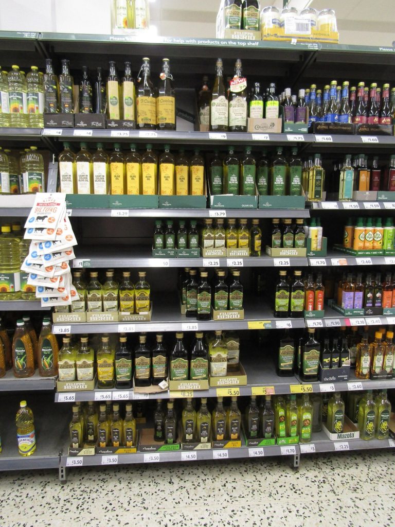 Shelves of olive oil and other cooking oils in a British supermarket, with own-label and branded bottles priced in pounds.