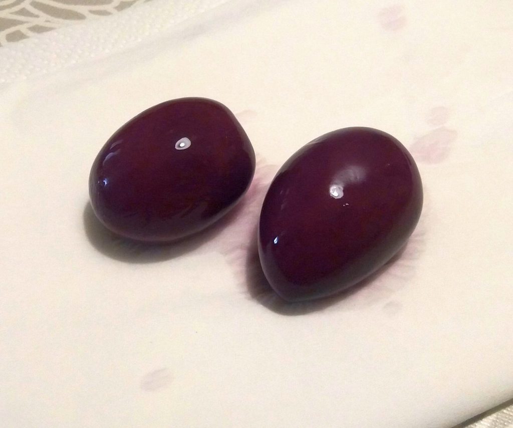 Two plump, deep purple Peruvian Botija olives resting on a white cloth.