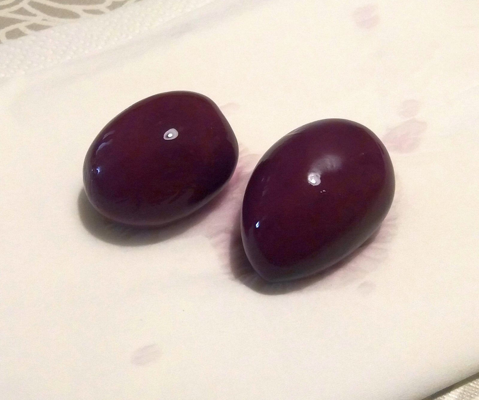 Two plump, deep purple Peruvian Botija olives resting on a white cloth.