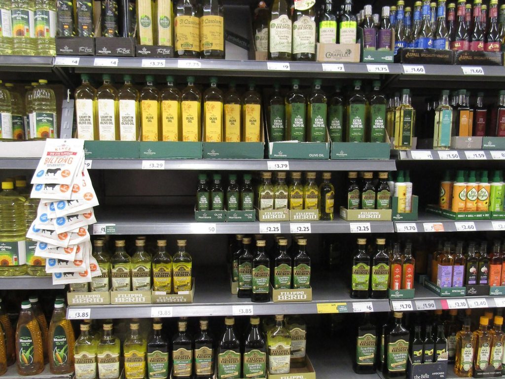 A supermarket shelf of cooking oils showing own-label bottles marked light in colour olive oil, olive oil and extra virgin olive oil side by side.