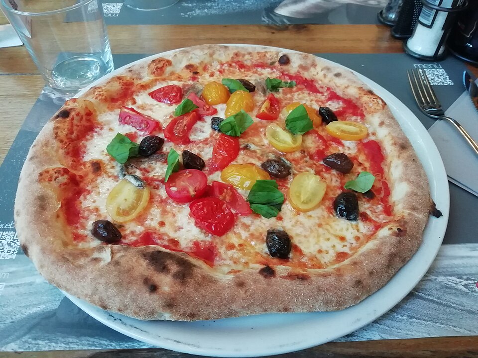 Wood-fired pizza topped with black olives, cherry tomatoes and fresh basil