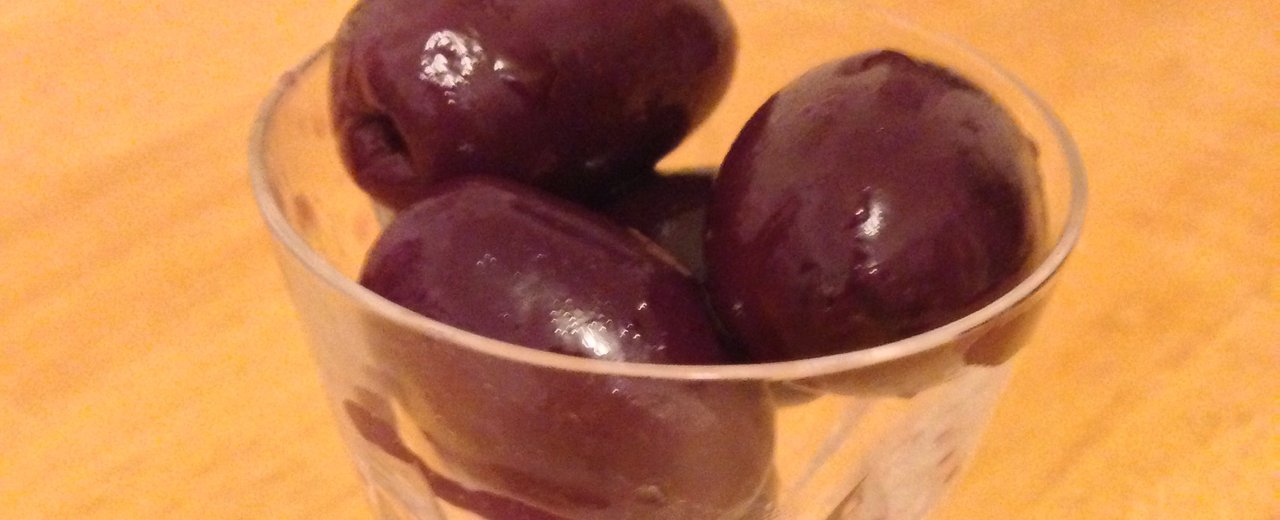 Large dark purple Alfonso table olives in a glass dish